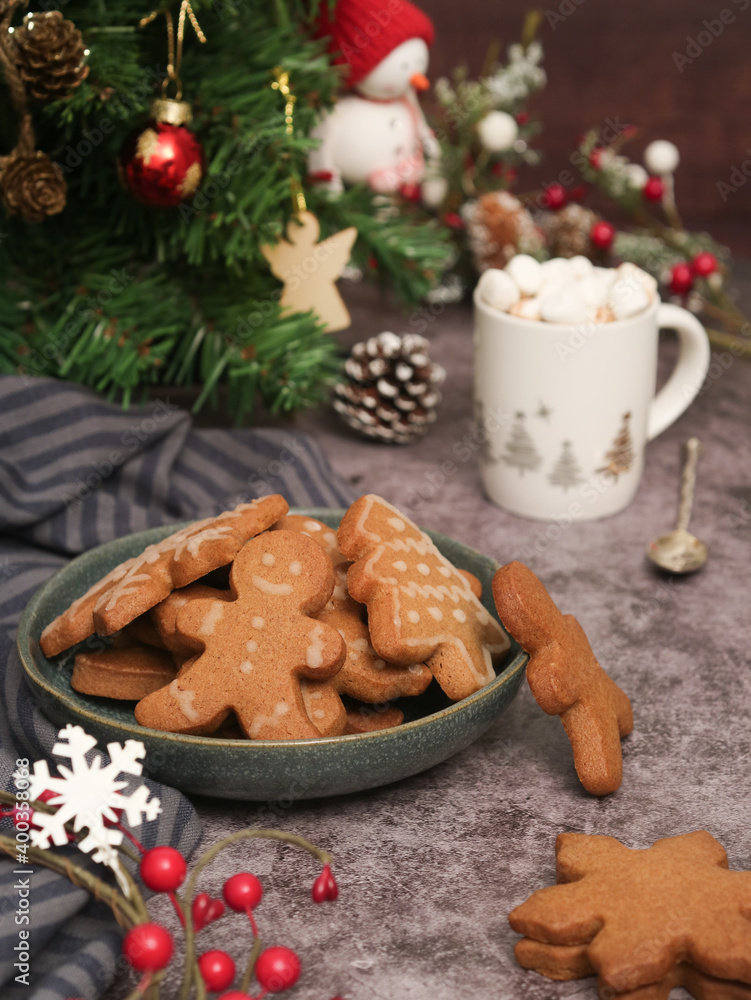 A plate of various Christmas sugar cookies decorated with royal icing and a cup of hot chocolate in and xmas tree in background. With cozy atmosphere holidays greetings festive