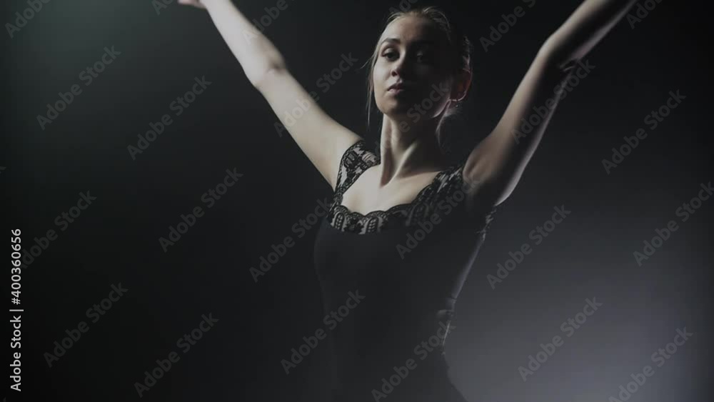 Young woman ballerina in black dress slowly turning around on the smoky stage Young woman ballerina in black dress slowly turning around on the smoky stage