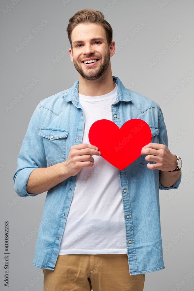 Portrait of charming man hold hand paper heart shaped card wear casual style shirt isolated over grey background Portrait of charming man hold hand paper heart shaped card wear casual style shirt isolated over grey background