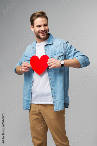 Portrait of charming man hold hand paper heart shaped card wear casual style shirt isolated over grey background © Anatoly Repin