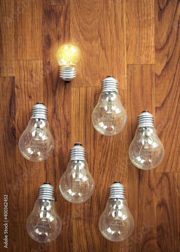 Fotografia glowing bulb uniqueness concept. many bulbs on brown wooden table