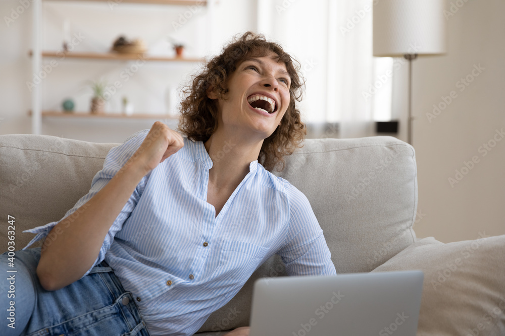 Overjoyed happy young woman lie on sofa before laptop screen shout in delight read email receive good job proposition. Laughing excited female freelancer celebrate getting money reward for great work Overjoyed happy young woman lie on sofa before laptop screen shout in delight read email receive good job proposition. Laughing excited female freelancer celebrate getting money reward for great work