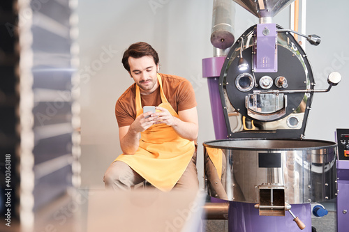 Worker using smartphone while locating near coffee roaster