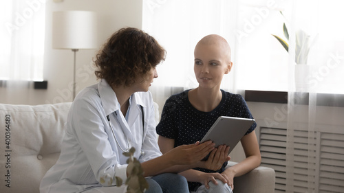 Confident doctor and woman patient discuss test results on pad screen on appointment at oncological center. Qualified physician explain treatment plan to young female sick with cancer using tablet pc photo