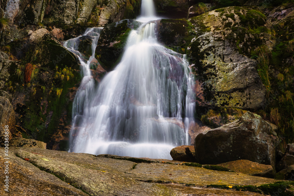 Fototapeta premium Autumn long exposure of creek Black (Big) Stolpich waterfalls in Jizera Mountain. Water falls into a deep forest canyon full of granite stones and rocks covered with green moss. Czech Republic