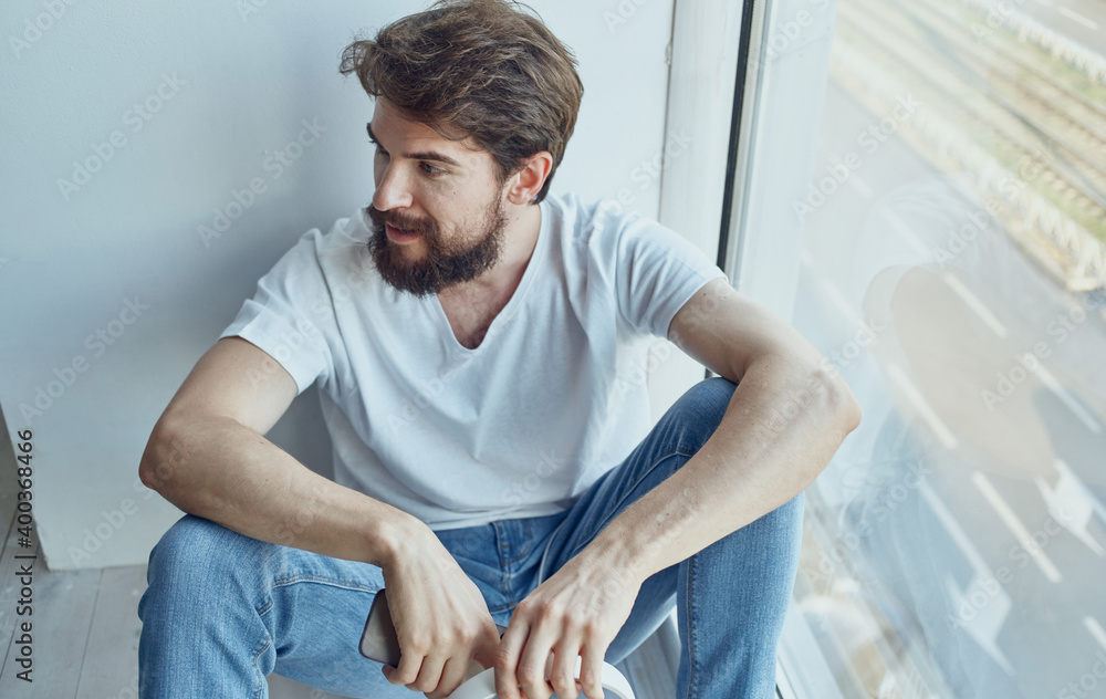 A man sits on a windowsill with a phone rest internet communication