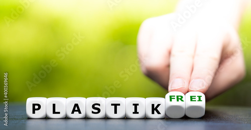 Hand turns dice and changes the German expression "plastik" (plastic) to "plastik frei" (plastic free).