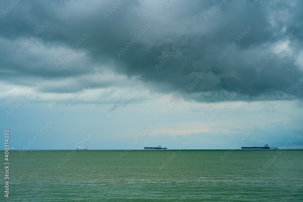 Seaview with ships in Port Dickson. Heavy clouds in the rainy season. The image contains soft focus, noise and grain.