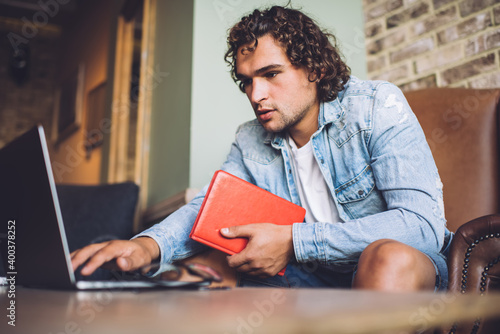 Serious caucasian male student in jeans jacket searching information for homework task using technology and wireless internet, concentrated skilled hipster guy freelancer typing on laptop computer