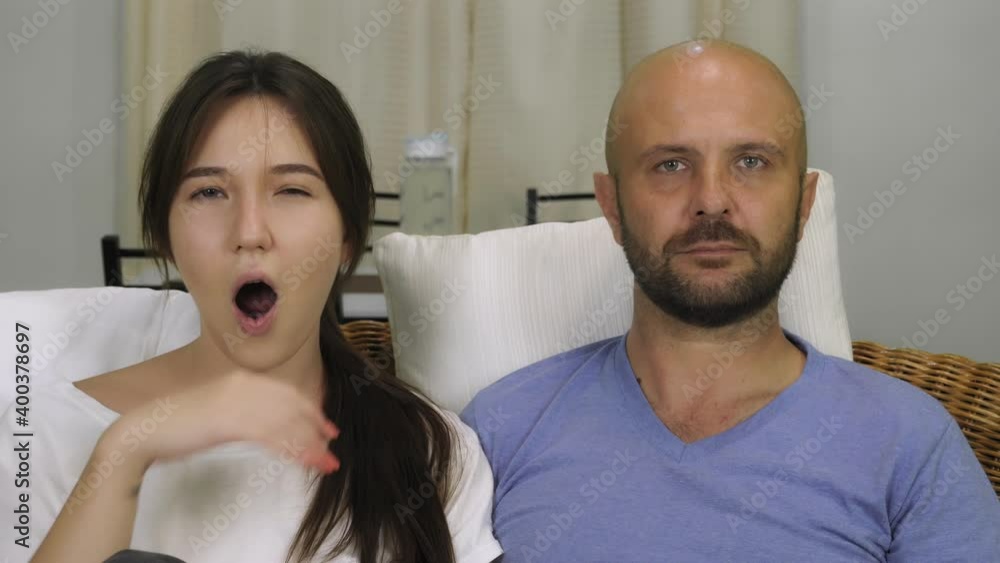 A man and a woman are sitting on the couch and watching TV. The man switches channels. Woman yawns. High quality 4k footage A man and a woman are sitting on the couch and watching TV. The man switches channels. Woman yawns. High quality 4k footage