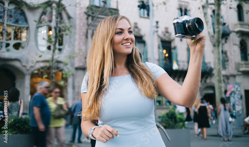 Cheerful Caucasian tourist using vintage technology for photographing architecture landscape near Casa Batllo in Barcelona, carefree woman taking pictures of city beauty in Hispanic Catalonia