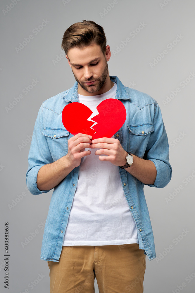 handsome young man holding broken paper red valentine heart standing over grey background handsome young man holding broken paper red valentine heart standing over grey background