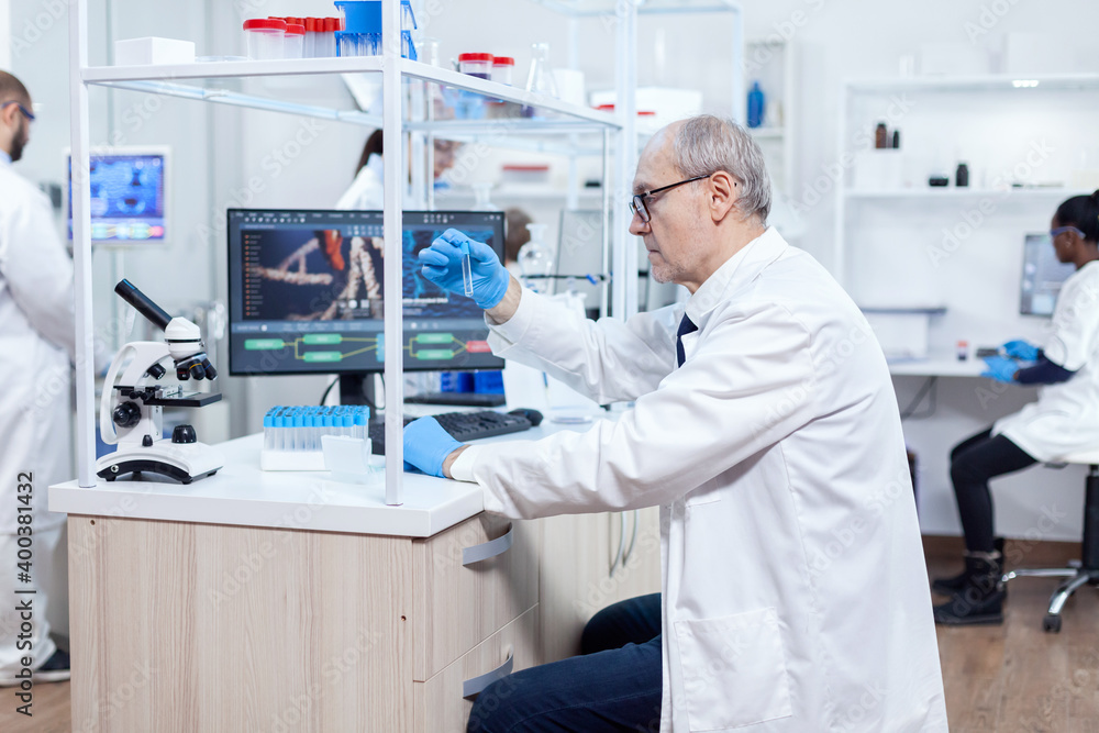 Senior scientist analysing and holding micobiology test tube in busy laboratory. Viorolog researcher in professional lab working to discover medical treatment. Senior scientist analysing and holding micobiology test tube in busy laboratory. Viorolog researcher in professional lab working to discover medical treatment.