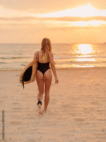 Young surfer woman on beach with surfboard at warm sunset. Attractive surfgirl on beach