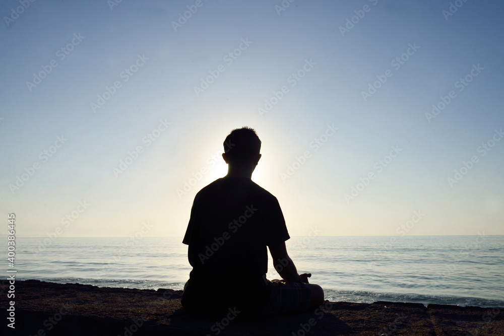 Silhouette of an Indonesian man meditating at the seaside of Matahari beach in Bali, Indonesia.