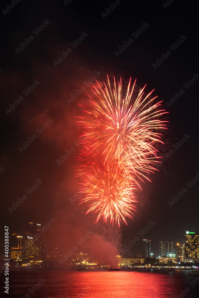 Vertical image beautiful sparkling colorful fireworks at night sky with cityscape and sea on background.