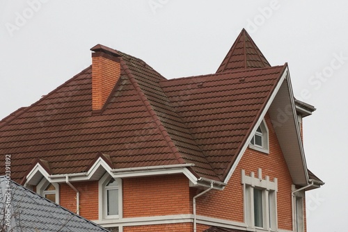 brick house with white windows and brown tiled roof with chimneys against gray sky