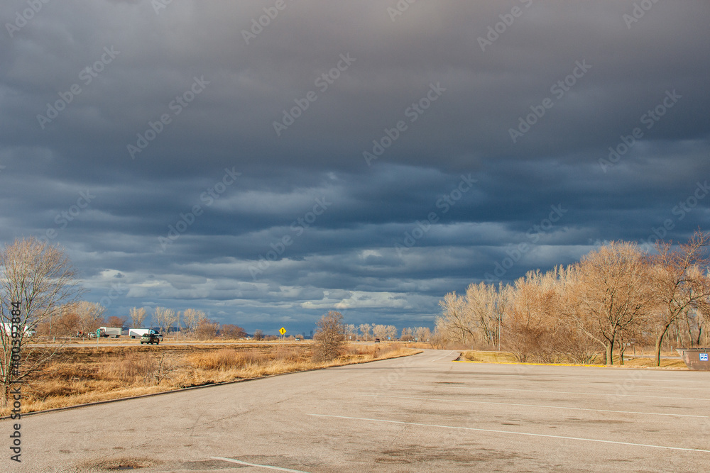 Beautiful dark blue sky over the highway. A landscape with a very unusual sky, trees without leaves and an asphalt road on an autumn day before a thunderstorm. Pacific Junction, IA, USA, 11-30-2019