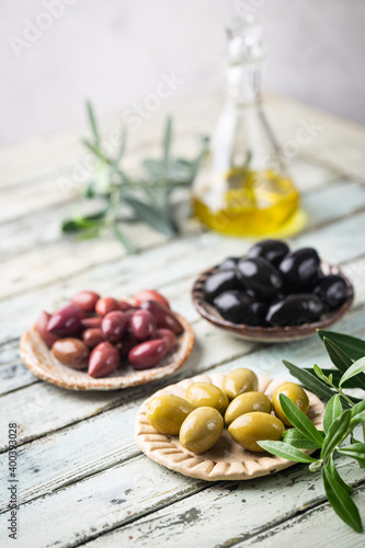 Variety of black and green olives and olive oil in bowls on white background close up