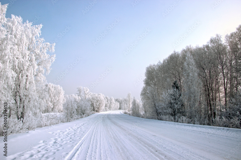 Winter landscape in silver tones. The wide snow covered road turns right and trees dressed in the silver along both edges of the road. Winter landscape in silver tones. The wide snow covered road turns right and trees dressed in the silver along both edges of the road.