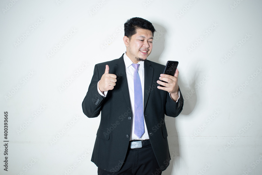 Portrait of a smiling businessman dressed in suit purple necktie is working on mobile phone in white background.
Portrait of a smiling businessman dressed in suit purple necktie is working on mobile phone in white background.
