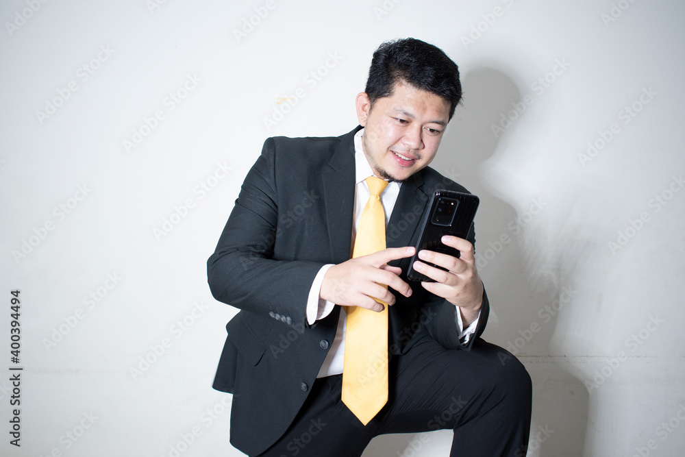 Portrait of a smiling businessman dressed in suit Yellow tie is working on mobile phone in white background. Portrait of a smiling businessman dressed in suit Yellow tie is working on mobile phone in white background.