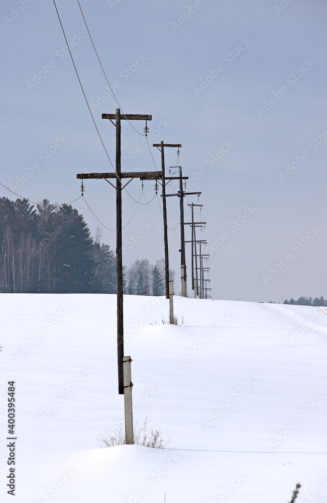 Power line poles stretch along the edge of the forest and disappear over the horizon. Winter landscape.