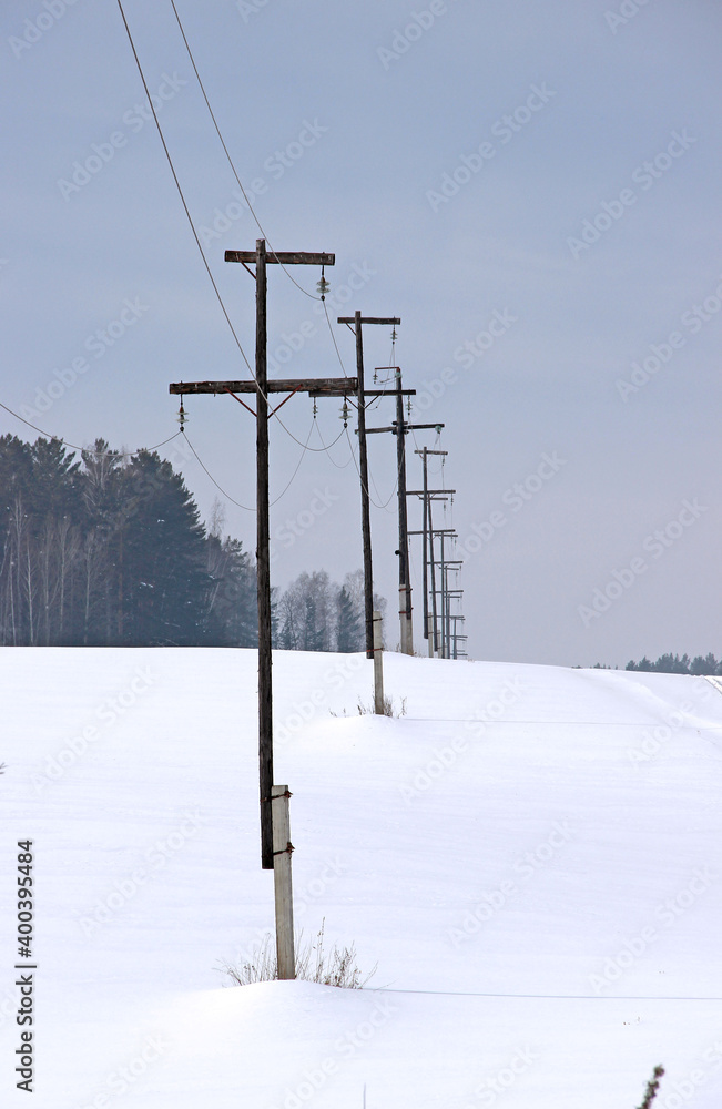 Power line poles stretch along the edge of the forest and disappear over the horizon. Winter landscape. Power line poles stretch along the edge of the forest and disappear over the horizon. Winter landscape.