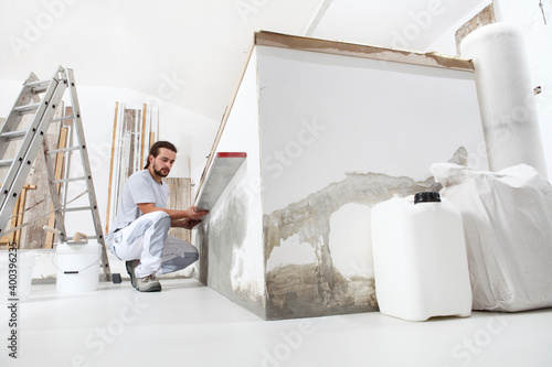 construction worker plasterer man looks at the spirit level and checks the wall in building site of home renovation with tools and building materials on the floor