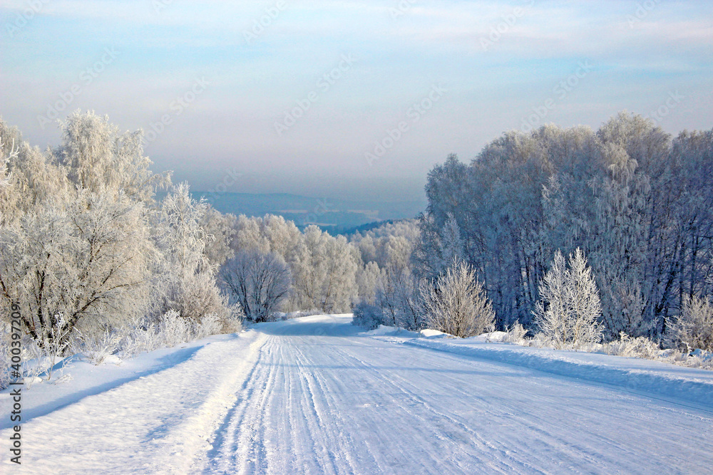 Clear winter day. Clear frosty blue sky. The road turns into the sparkling silver forest.