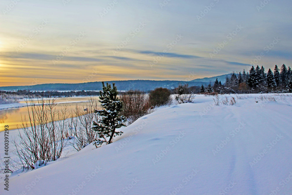 View on a snow covered river bank and wooded mountains in the twilight.