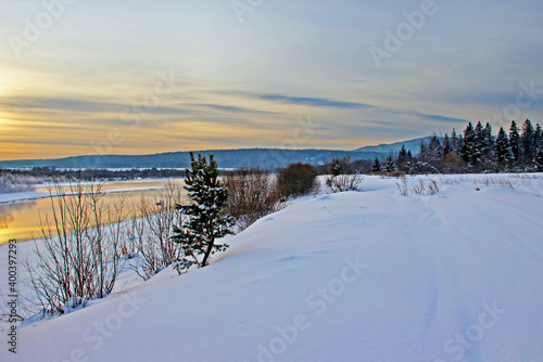 View on a snow covered river bank and wooded mountains in the twilight. © Pavel