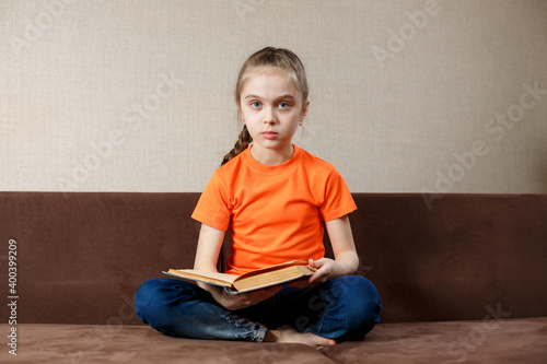 Little girl with book on her legs looking at camera