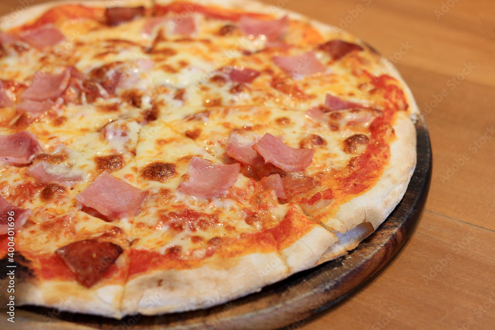 Sliced cheesy pizza on wooden cutting board.Delicious Italian food delivered in cardboard box for lunch meal.Crusty thin dough baked in oven with tasty parmesan,gorgonzola,mozzarella,ham and cheese