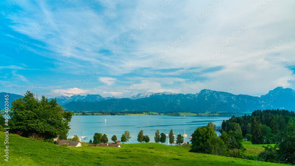 Germany, Allgaeu, Boats and sailing ships on silent water of forgensee lake with spectacular alps panorama at sunset in summer
