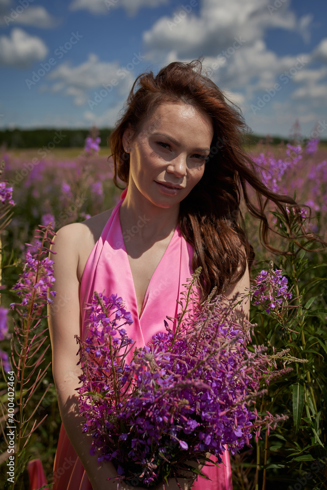 Smiling young woman with dark long hair holding the bouquet of pink flowers. Pink Ivan Tea or blooming Sally in the field Smiling young woman with dark long hair holding the bouquet of pink flowers. Pink Ivan Tea or blooming Sally in the field