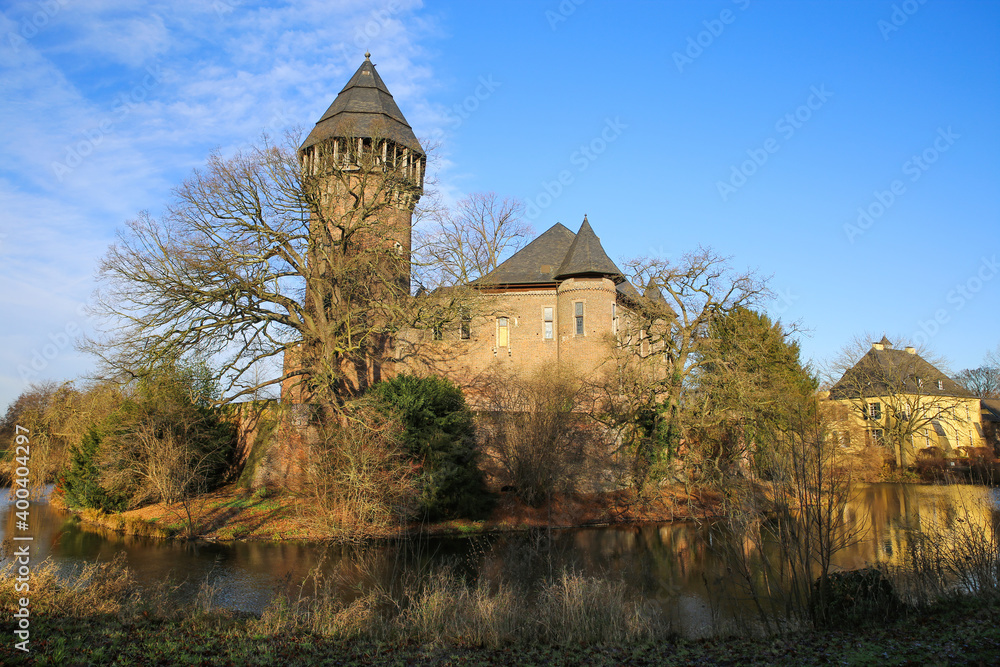 Panoramic view over moat on medieval ancient water castle and defensive towerfrom 12th century with bare trees in winter against blue sky - Krefeld Linn, Germany