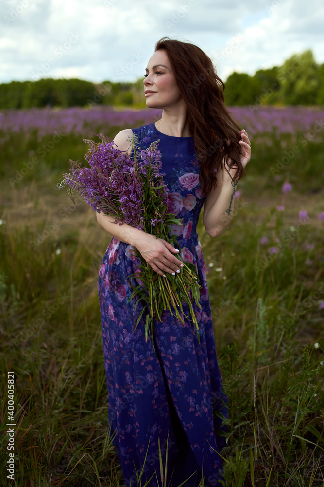 Smiling young woman with dark long hair holding the bouquet of pink flowers. Pink Ivan Tea or blooming Sally in the field Smiling young woman with dark long hair holding the bouquet of pink flowers. Pink Ivan Tea or blooming Sally in the field