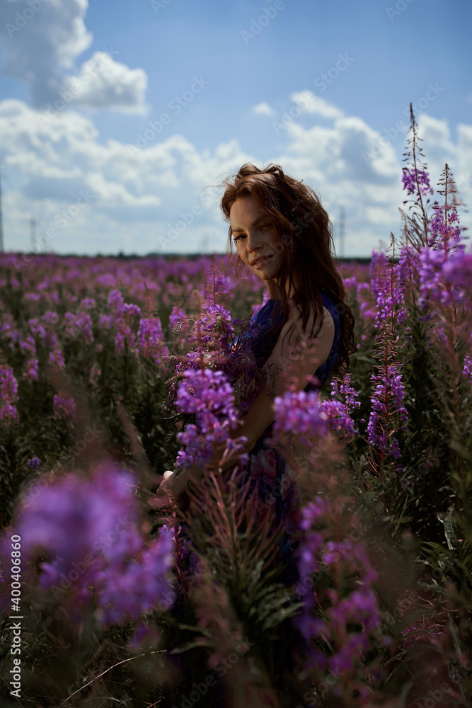 Smiling young woman with dark long hair holding the bouquet of pink flowers. Pink Ivan Tea or blooming Sally in the field Smiling young woman with dark long hair holding the bouquet of pink flowers. Pink Ivan Tea or blooming Sally in the field