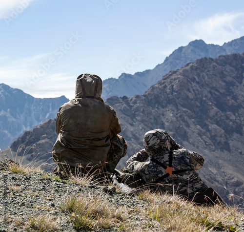 Two men in camouflage with weapons are watching in the mountains.