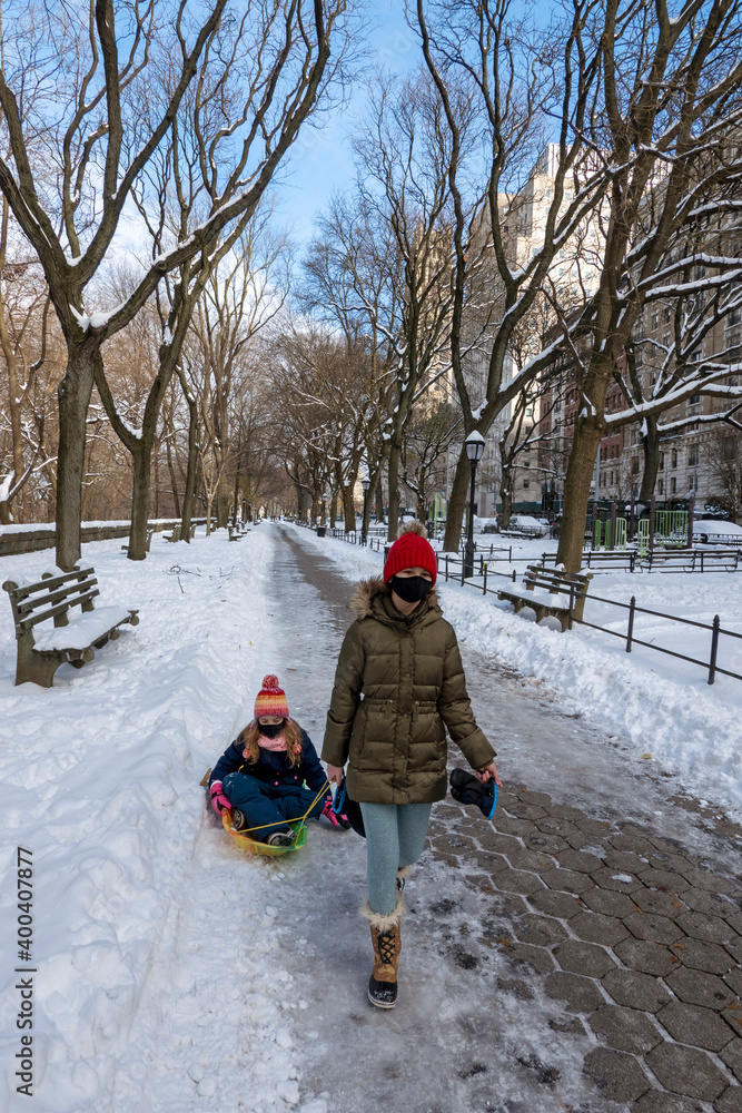 New York, USA, December 2020. Young girls wearing masks with their sled