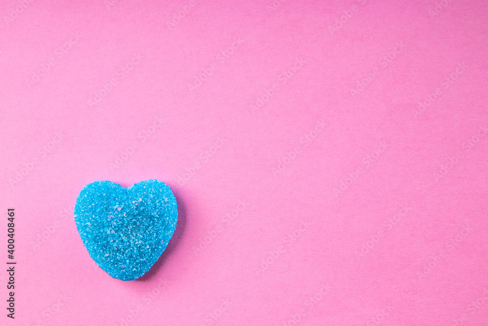 Blue heart shaped gummi candy on pink background, free space for text