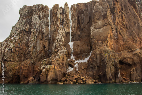 A stone cliff rises from the water on Deception Island in Antarctica. Frozen waterfall.