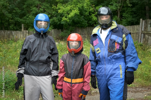 Portrait of mom, dad and son in costumes and helmets to fly in aerodynamic tube. Entertainment in the fresh air, flying in aerodynamic tube. Outdoors activity. They are preparing to fly.