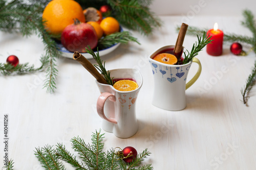 christmas mulled wine in heart shaped cups, spice, plate with fruits, fir tree branches, burning candle, new year decoration on white background