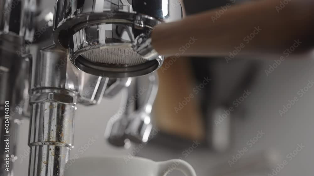Slow motion low angle shot of coffee extraction with naked portafilter into white cup Slow motion low angle shot of coffee extraction with naked portafilter into white cup