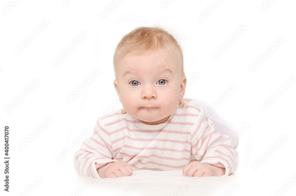Interested cutest little 4 month old caucasian baby girl in striped T-shirt looking at camera lying on stomach on white background, isolated. Copy space. Interested cutest little 4 month old caucasian baby girl in striped T-shirt looking at camera lying on stomach on white background, isolated. Copy space.