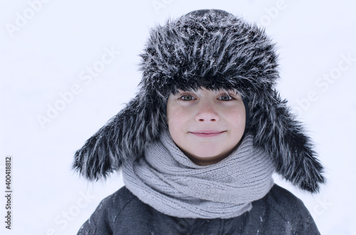 Happiness caucasian smilling boy with a fluffy hat outside in the snow at winter, snowdrift. The concept of winter rest, leisure, people, vacation, outdoor games in the snow, winter time 