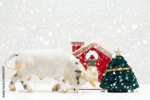 Toy bull, a symbol of the new year 2021, a toy house at the Christmas tree. Winter, it's snowing. Happy New Year. Greeting card ideas. Copy space. Mock up