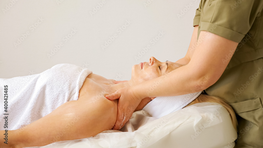 Experienced cosmetologist massages woman bare shoulders and neck lying on large couch of white colour in beauty salon ward close view Experienced cosmetologist massages woman bare shoulders and neck lying on large couch of white colour in beauty salon ward close view
